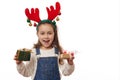 Overjoyed cheery child girl, deer antler hoop, holding out at camera happy presents for Christmas or New Year