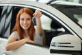 Overjoyed driver woman smiling and showing new key while sitting in car showroom Royalty Free Stock Photo