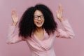 Overjoyed emotional female entrepreneur raises hands, laughs sincerely, wears spectacles and formal jacket, works in business