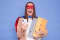 Overjoyed extremely happy brown haired woman wearing superhero costume holding paper folders posing isolated over blue background