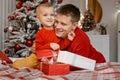 Overjoyed father hugs his charming little son sitting on bed with present boxes near the Christmas tree Royalty Free Stock Photo