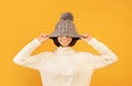 Overjoyed lady pulling down grey woollen hat and smiling, fooling and posing to camera over yellow background