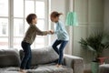 Overjoyed little boy and girl holding hands, jumping on couch