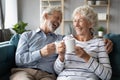 Overjoyed mature family couple laughing at jokes, drinking morning coffee.