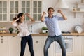 Overjoyed millennial couple dance in home kitchen