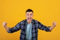 Overjoyed millennial guy screaming in excitement, gesturing YES with both hands on orange studio background