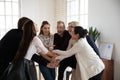 Overjoyed multiracial employees stack hands involved in teambuilding activity