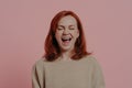 Overjoyed red-haired woman laughing positively, with closed eyes, isolated on pink background