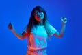 Overjoyed, relaxed Asian woman dancing raising hands against blue gradient studio background in neon light.