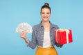 Overjoyed satisfied buyer, happy fashionably dressed woman with hair bun holding gift box and dollar money