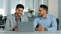 Overjoyed smiling male employees looking at laptop screen, excited by unbelievable good news. Happy coworkers