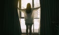 Overjoyed young beautiful woman standing by bedroom and opening curtains look in window distance meet welcome new day. Royalty Free Stock Photo