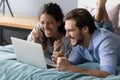 Overjoyed young couple lying on bed, looking at laptop screen. Royalty Free Stock Photo