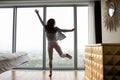 Overjoyed young female dancing at picture window of luxury hotel