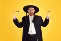 Overjoyed young Jewish man with widely open mouth holds groggers in hands against sunny yellow background. Purim Royalty Free Stock Photo