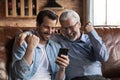 Overjoyed young man aged father raise fists look at phone