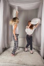 Overjoyed young mom and happy little daughter have fun engaged in pillow fight in bedroom, excited mother and small preschooler