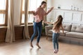 Overjoyed young mom and little daughter dancing in living room