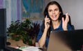 Overjoyed young woman in denim shirt working home with a laptop, talking via phone and looks up. World map in the Royalty Free Stock Photo