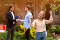 Happy young woman with house key and her husband shaking hands with realtor in backyard Royalty Free Stock Photo