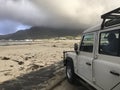 An overlanding vehicle stops on the beach with heavy cloud overhead Royalty Free Stock Photo