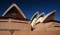 Stacked white shells of curved and pointy roofs with exposed concrete beams on large pink podium of Sydney Opera House Australia