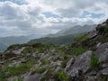 Overlook of the Gap of Dunloe trail with rocks and sparse green vegetation, extending to a distant mountain range under a cloudy Royalty Free Stock Photo
