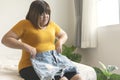 Oversize woman want to wear short jeans. Overweight female sitting on the bed holding pants jeans worried about weight gain Royalty Free Stock Photo
