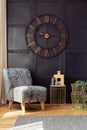 Oversized wall clock, armchair and golden table with a vase in a living room interior. Real photo