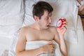 Oversleep concept. Young man is waking up and looking on alarm clock. Royalty Free Stock Photo