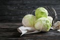 Overturned metal basket with fresh cabbages on wooden table