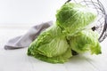 Overturned metal basket with fresh ripe cabbage on light wooden table