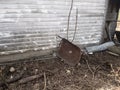 Overturned metal wheelbarrow with hole in center leaning against wall