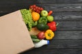 Overturned paper bag and groceries on black wooden background