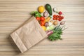 Overturned paper bag with vegetables, herbs and bottle of juice on wooden background