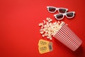 Overturned paper cup with popcorn, cinema tickets and 3D glasses on red background, flat lay. Space for text Royalty Free Stock Photo