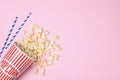 Overturned paper cup with tasty popcorn on color background, top view.