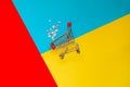 Overturned shopping trolley and scattered medicine pills on multicolored background. Concept of medicine, healthcare and pharmacy