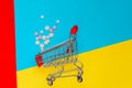 Overturned shopping trolley and scattered medicine pills on multicolored background. Concept of medicine and pharmacy