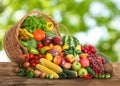 Overturned wicker basket with different fresh organic vegetables and fruits on wooden table against blurred green background Royalty Free Stock Photo