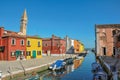 Overview of colorful buildings, bell tower and boats facing a canal at Burano.