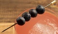 Overview mixed drink cocktail with four blueberries and square ice cube with a wooden background