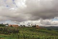 Overview of vineyards and hills with villa at the top in the Tuscan countryside.