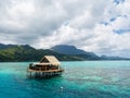 Lonely overwater bungalow of black pearl farmers. Blue azure turquoise lagoon. Raiatea island, French Polynesia. Aerial view.