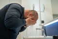 Overweight balded man washing face in bathroom at home under sink, side view.