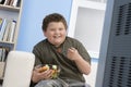 Overweight Boy Eating Bowl Of Fruit In Front Of TV