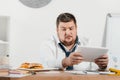 overweight businessman looking at junk food while working with tablet Royalty Free Stock Photo