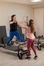 Overweight caucasian woman doing pilates exercises on reformer with personal trainer. Royalty Free Stock Photo