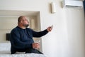 Overweight exhausted man drinks water switches on air conditioner at home in summer.