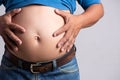 Overweight or fat adult man hand holding belly stomach in very tight jeans on a gray background. Healthcare, medicine concept Royalty Free Stock Photo